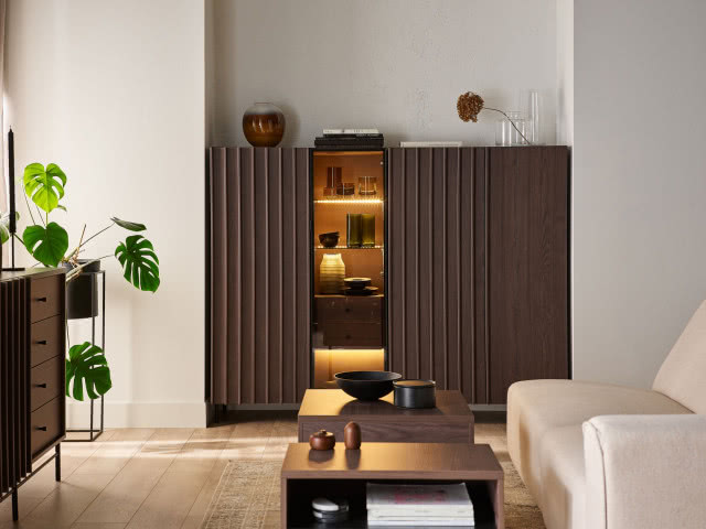 Komoda z ryflowanymi frontami w stylu mid-century, ciemne drewno i podświetlana witryna w minimalistycznym salonie z rośliną i stolikiem