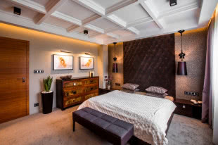 Ściana za łóżkiem w sypialni jest pokryta brązowym pikowanym pluszem.