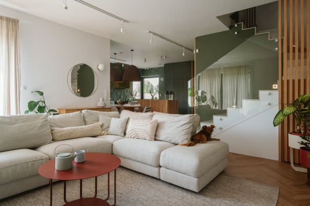 Beżowa sofa w salonie na tle zielonej kuchni