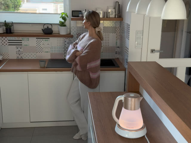 kobieta czekająca aż woda w czajniku się zagotuje, drewniane blaty kuchenne