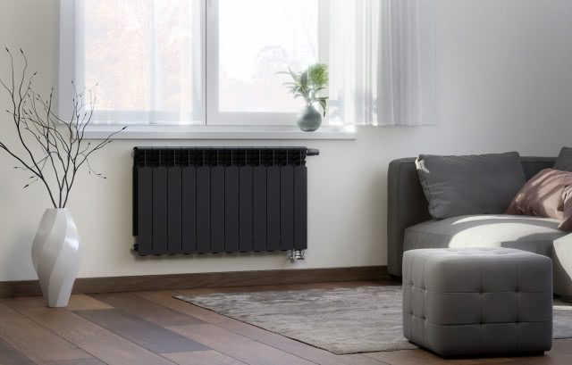 Grzejniki aluminiowe G500F od KFA Armatura mają 20 lat gwarancji, kanapa, puf, poduszki ozdobne, drewniana podłoga, wazon z gałęziami, na oknie wazon z kwiatami, firany, dywan