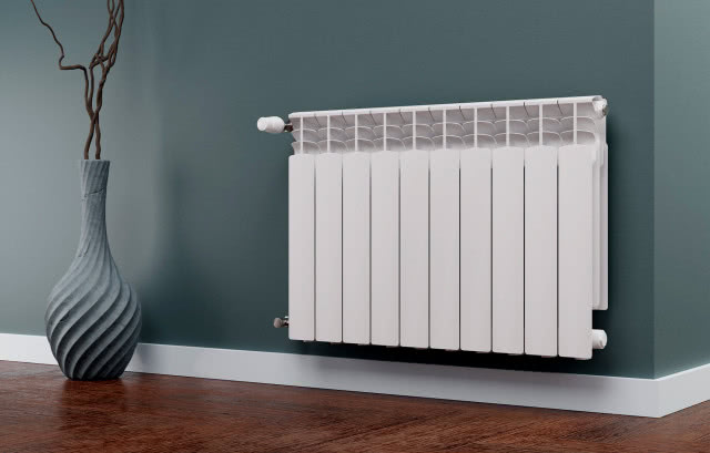 Kierownice powietrza w grzejniku aluminiowym G500F KFA Armatura, wazon z gałęziami, drewniana podłoga, szare ściany, biała listwa przypodłogowa