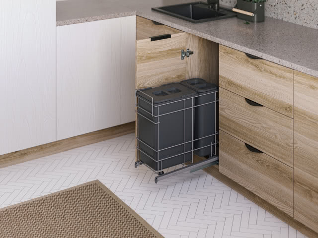 kosze do segregacji śmieci, drewniane fronty kuchenne, czarny zlewozmywak, na podłodze biała jodełka, beżowo-brązowy dywan, białe fronty kuchenne