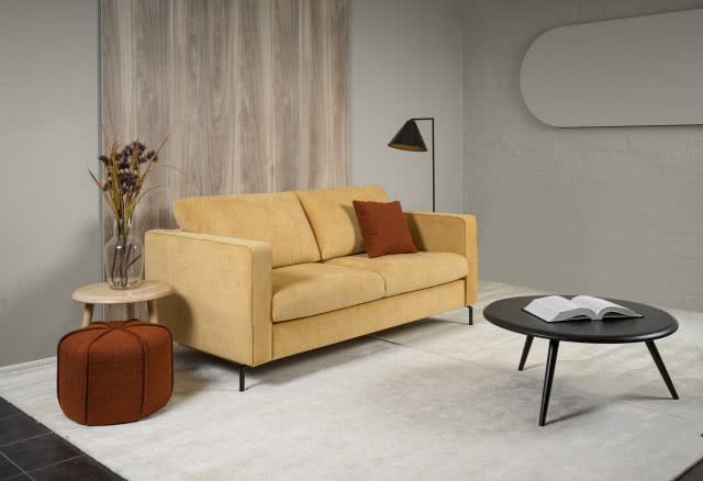 żółta sofa, puf, stolik, wazon, lampa podłogowa, dywan, drewno na ścianie