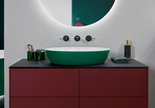 owalna umywalka w kolorze zielony,, okrągłe podświetlane lustro, brązowe meble łazienkowe, bateria podtynkowa, kosmetyki