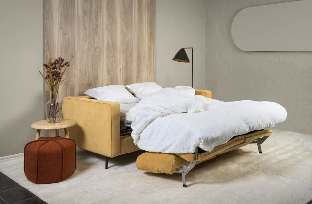 żółta sofa, puf, stolik, wazon, lampa podłogowa, dywan, drewno na ścianie