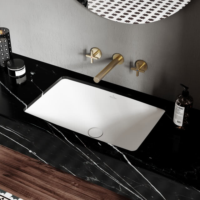 prostokątna umywalka wpuszczona w blat, czarny blat z marmuru, złota bateria umywalkowa podtynkowa, okrągłe lustro, kosmetyki