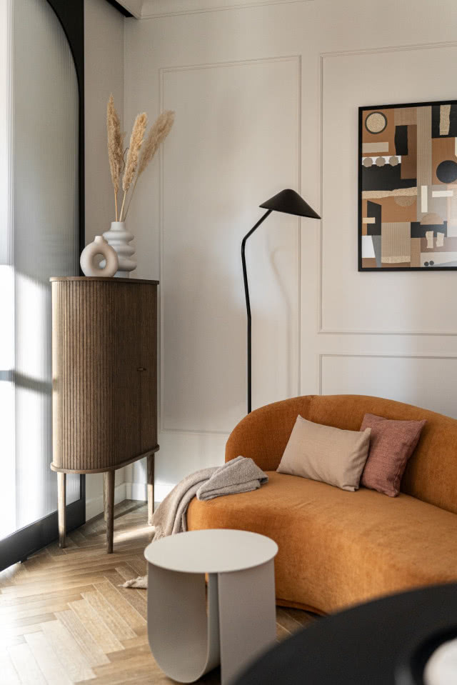 Pomarańczowa kanapa na tle białej sztukaterii w salonie