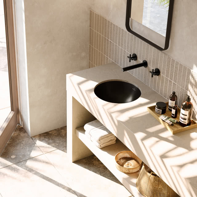 czarna umywalka wpuszczana w blat, czarna bateria podtynkowa, blat z marmuru, ręczniki, koszyki wiklinowe, taca, kosmetyki, prostokątne lustro w czarnej ramie