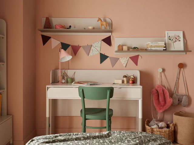 białe biurko z szufladami, zielone krzesło, półki wiszące nad biurkiem