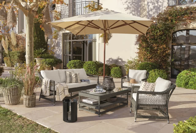 parasol z nogą centralną, pod nim rattanowe meble i takie same donice