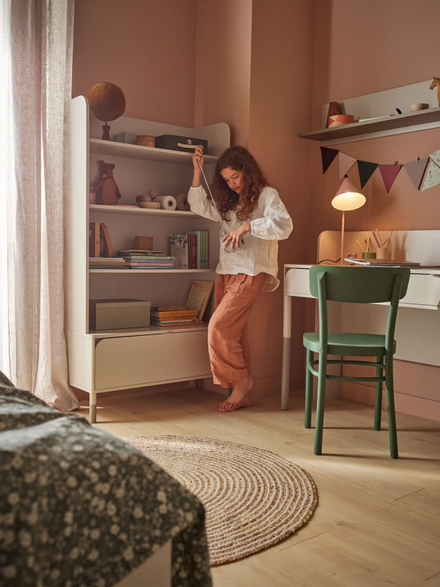 biurko, zielone krzesło, okrągły dywanik, zasłony, półki, łóżko, lampka na biurku, proporczyki