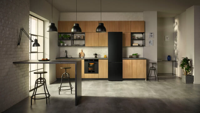 lodówka samsung, drewniane fronty kuchenne, czarny blat kuchenny, czarna bateria, duże okno, wyspa kuchenna, stołki, piekarnik, kwiaty w doniczkach, oświetlenie sufitowezlewozmywakowa, czarny zlewozmywak, cegła na ścianie