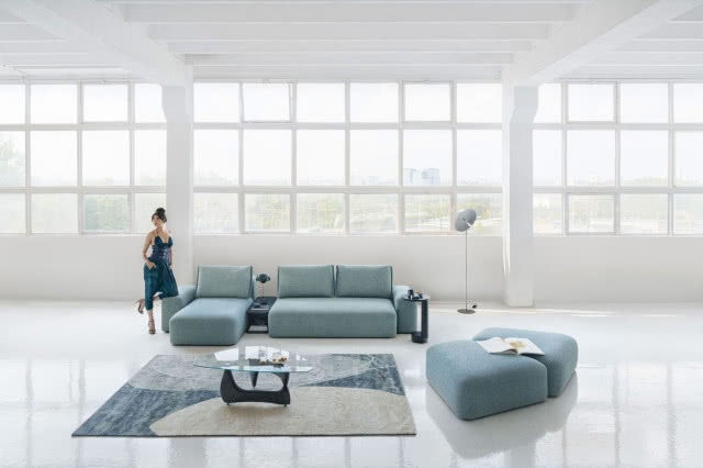 niebieska sofa, stolik kawowy, dywan w kolorze niebieskim, pufy, lampa podłogowa, lampa biurkowa, duże okno, białe ściany