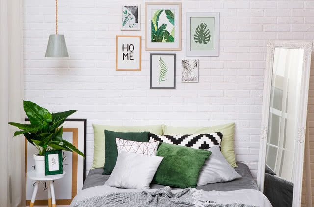 Sypialnia w stylu skandynawskim z zielonymi dekoracjami: poduszkami, obrazami na ścianie, roślinami