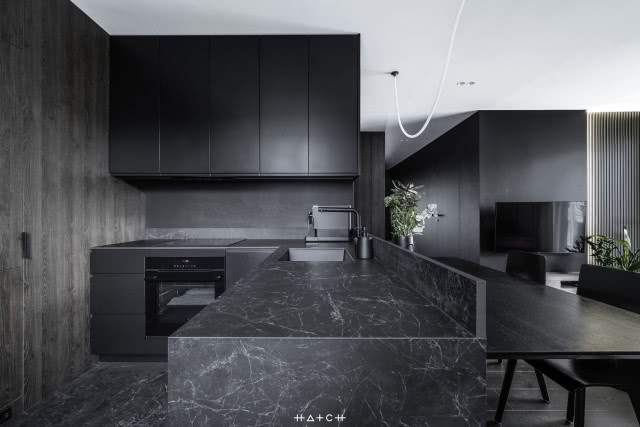 czarne meble kuchenne, półwysep, piekarnik, duży stół z krzesłami, telewizor, lamele na ścianie