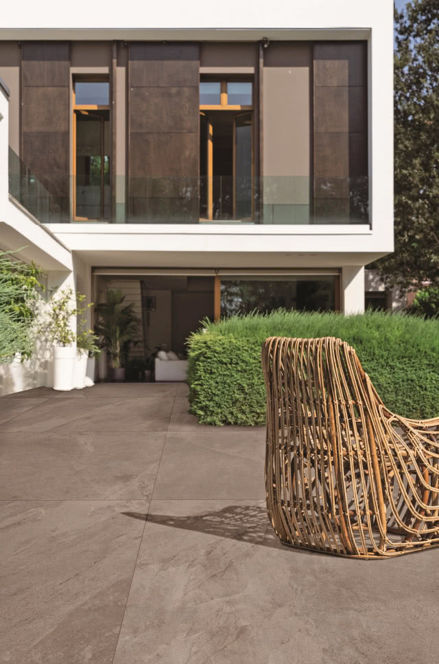 taras z ciemnego kamienia, na nim fotel, w tle nowoczesny dom