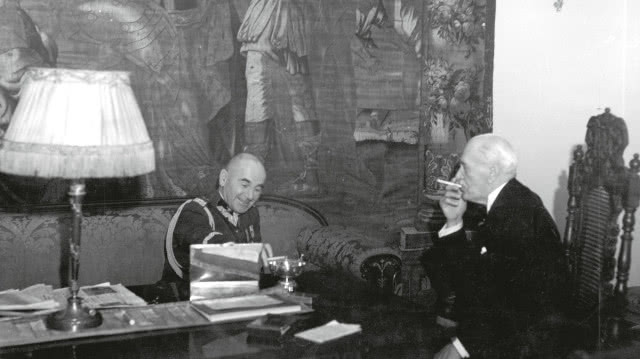 fotografia czarno-biała, dwóch mężczyzn siedzi swobodnie na kanapie, jeden z nich pai cygaro