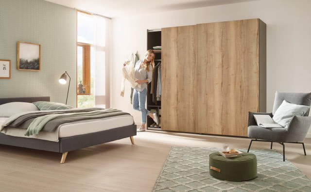 duża drewniana szafa z drzwiami przesuwnymi, duże łóżko, fotel, pufa, obrazy, lampa podłogowa