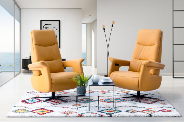 dwa żółte fotele obrotowe, stoliki kawowe, paproć w doniczce, lampa podłogowa, obraz, komoda, duże okno tarasowe, dywan