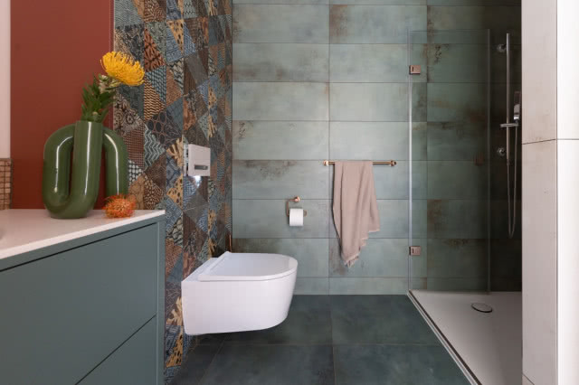 kabina prysznicowa, sedes podwieszany, kolorowe płytki na ścianie, wazon z kwiatkiem, uchwyt na ręczniki