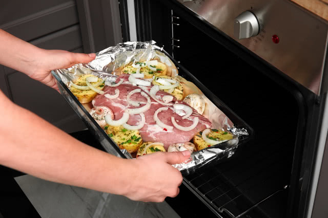 mężczyzna wkłada mięso w foremce wyłożonej folią aluminiową do piekarnika