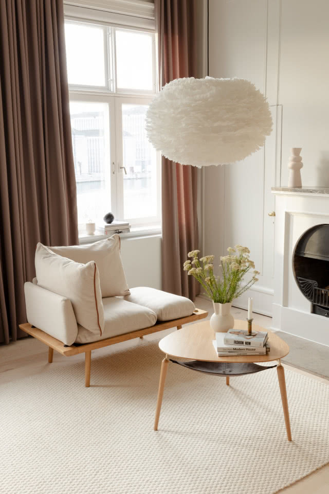 lampa z piórkami nad stolikiem, szezlongiem i kominkiem 