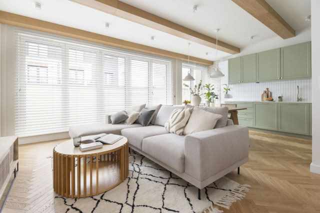 Drewniana podłoga w salonie z rattanowymi dodatkami i szarą kanapą