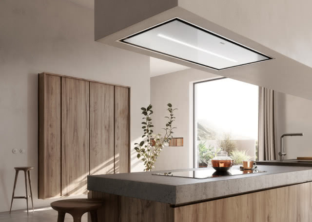 Franke, okap AirHub, drewniane szafki wiszące na ścianie, wyspa kuchenna, płyta grzewcza, kwiat, dzbanek z herbatą, filiżanka, bateria zlewozmywakowa, stołki