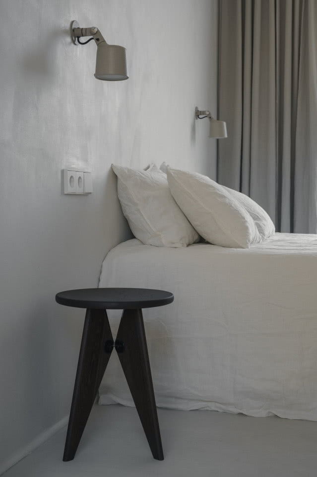 Czarny taboret na tle łóżka przykrytego białą narzutą.