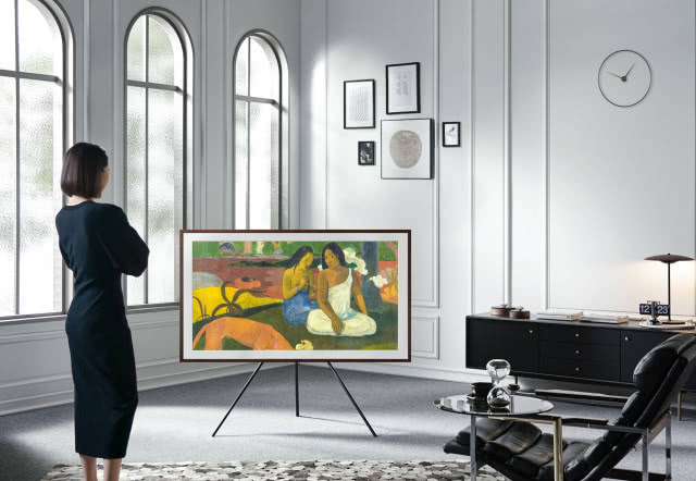 telewizor z platformą Art Store, białe ściany, obrazy, czarna komoda, stolik kawowy, fotel, szara wykładzina