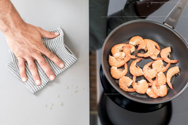 płyta indukcyjna, patelnia, krewetki, szary blat kuchenny, ścierka, tłuszcz