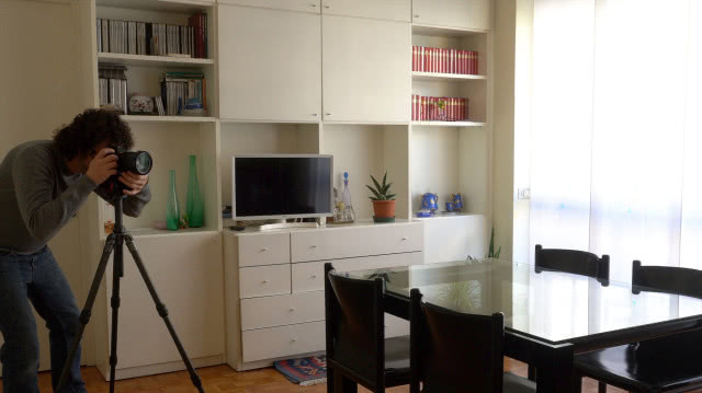 Fotograf wykonuje zdjęcia salonu z jadalnią, używając aparatu na statywie podczas sesji fotografii wnętrz.