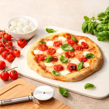 Domowa pizza margherita na kamieniu do pieczenia z pomidorami, mozzarellą i świeżą bazylią.