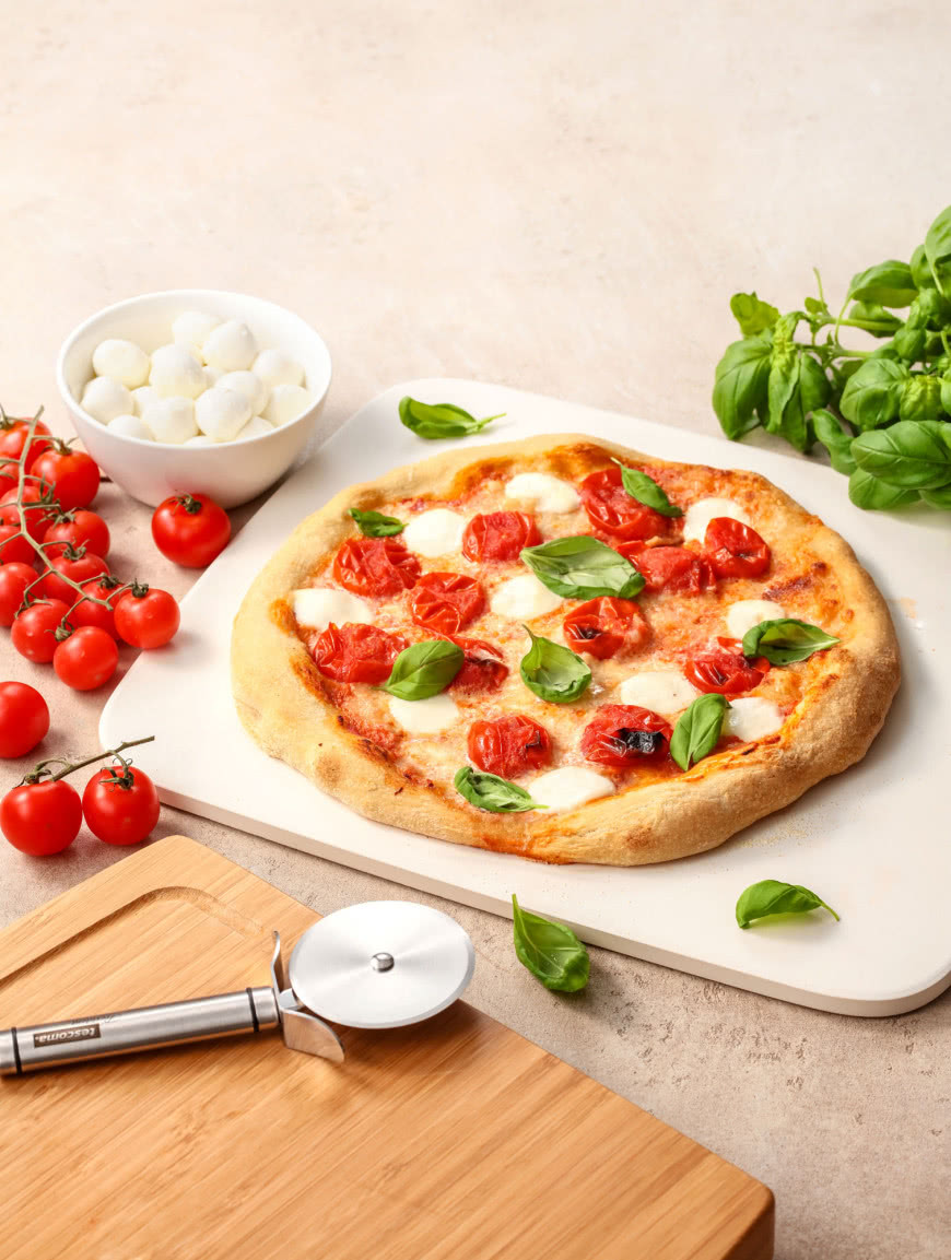 Domowa pizza margherita na kamieniu do pieczenia z pomidorami, mozzarellą i świeżą bazylią.