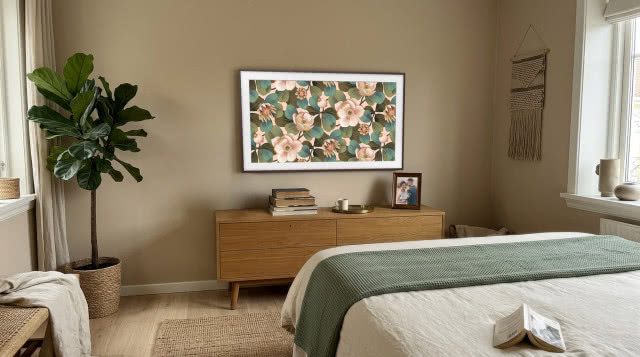 Samsung The Frame z kwiatową grafiką w sypialni inspirowanej naturą, z drewnianą komodą, rośliną, plecionkami i zielonymi tekstyliami.