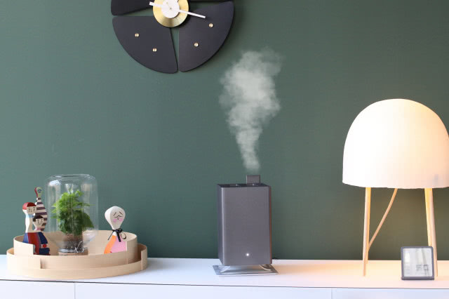 zielona ściana, komoda, nawilżacz, roślinka w słoiku, figurki, lampa na komodzie, zegar na ścianie