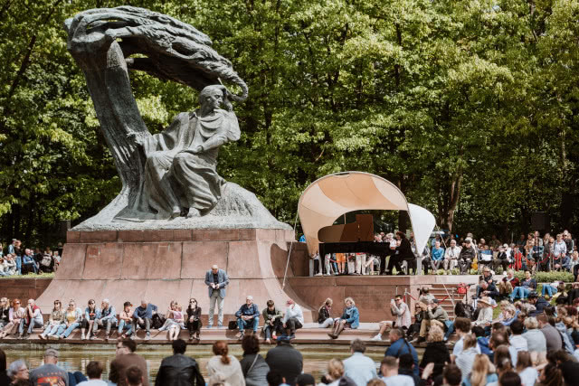 pomnik, namiot, pod którym grają pianiści i zebrana publiczność