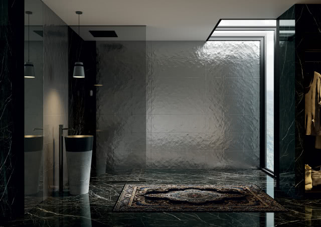 łazienka w tonacji ciemnej, ciemne płytki z połyskiem, umywalka, bateria umywalkowa wolnostojąca, dywan, kabina prysznicowa
