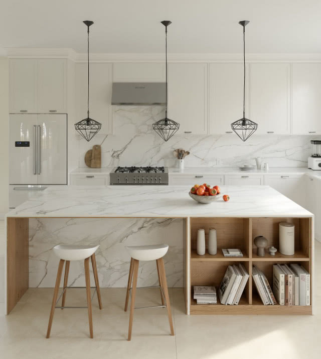 wyspa kuchenna z naturalnym kamieniem, stołki barowe, półki na książki, lodówka, oświetlenie sufitowe punktowe, płyta gazowa, białe meble kuchenne