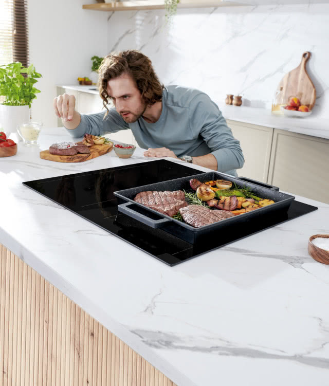 Precyzja w kuchni może mieć różne oblicza, na blaszce steki, ziemniaki pieczone, wyspa kuchenna, białe blaty, zioła, końcowa potrawa