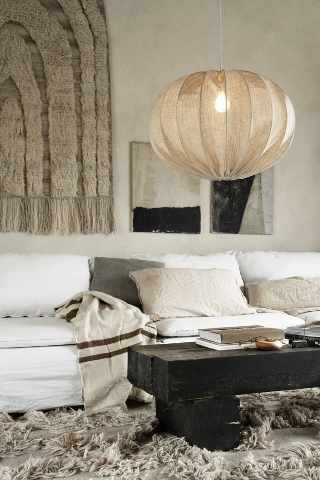 Lniana lampa wisząca w stylu boho i modern organic nad jasną sofą w przytulnym salonie w naturalnych odcieniach.