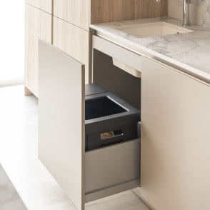 Nowoczesna kuchnia z wysuwanym systemem do segregacji odpadów ukrytym w szafce pod zlewem, zapewniającym wygodny dostęp.