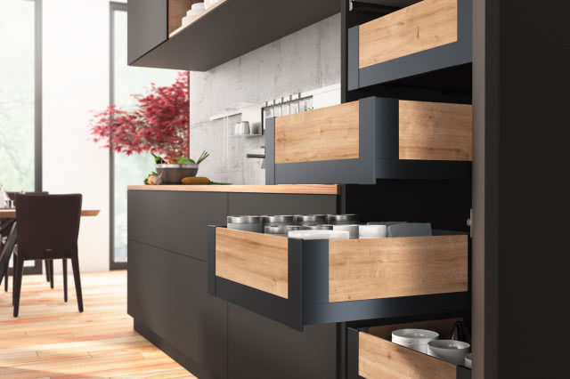szuflady z drewnianymi bokami, drewniana podłoga, czarne fronty kuchenne, beton na ścianie, stół z krzesłami