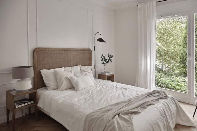 Jasna sypialnia ze sztukaterią na ścianach i zagłówkiem z plecionki