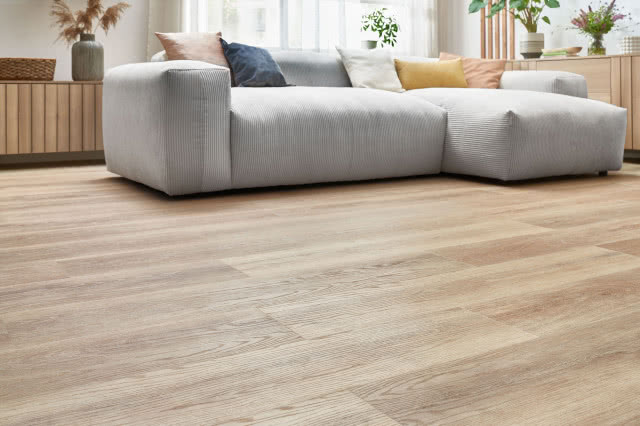 winylowe panele imitujące naturalne drewno, kanapa, poduszki ozdobne, komoda, kwiaty, firany, lamele