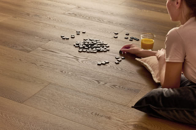 winylowe panele imitujące naturalne drewno, kobieta układająca kostki scrable, sok w szklance, poduszka