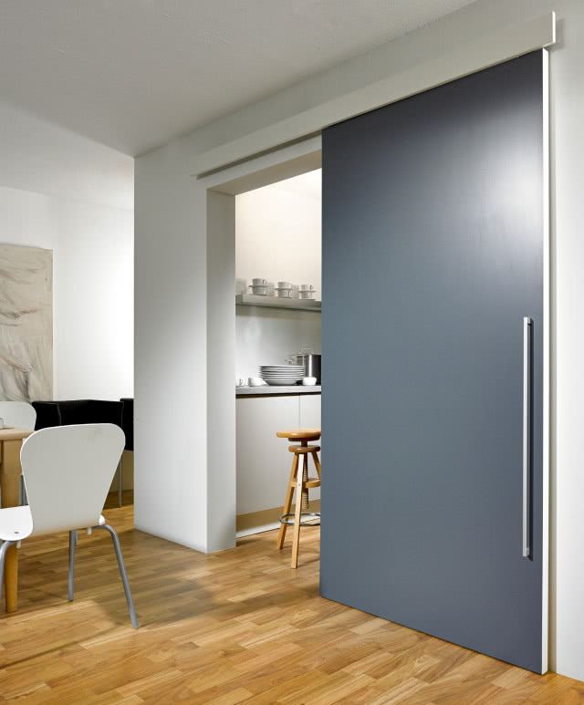 szare drzwi przesuwne, drewniana podłoga, białe krzesła, stołek, białe meble kuchenne, talerze, filiżanki