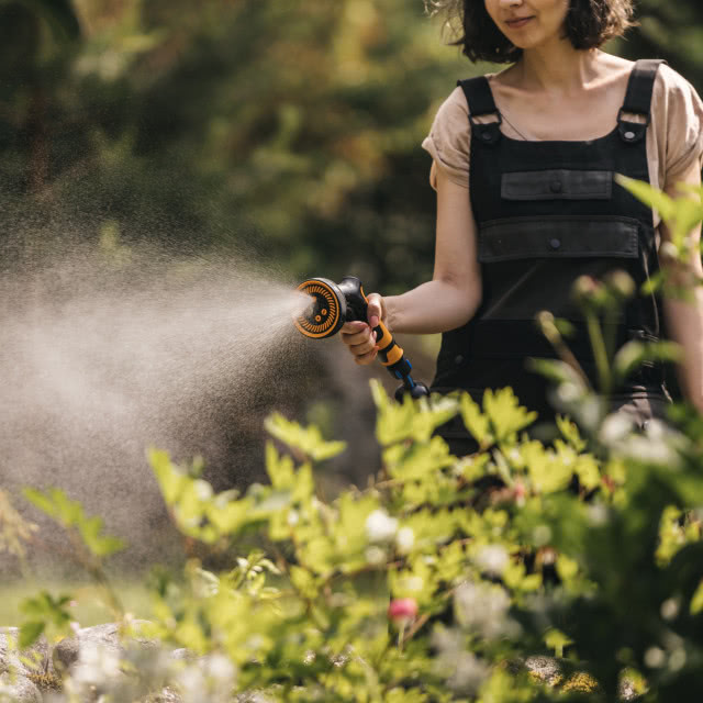 Kobieta podlewająca ogród, krzewy kwitnące, drzewa, ogrodniczki