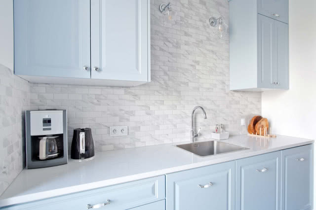 płytki cegiełki, niebieskie meble kuchenne z białym blatem, ekspres do kawy, kinkiety